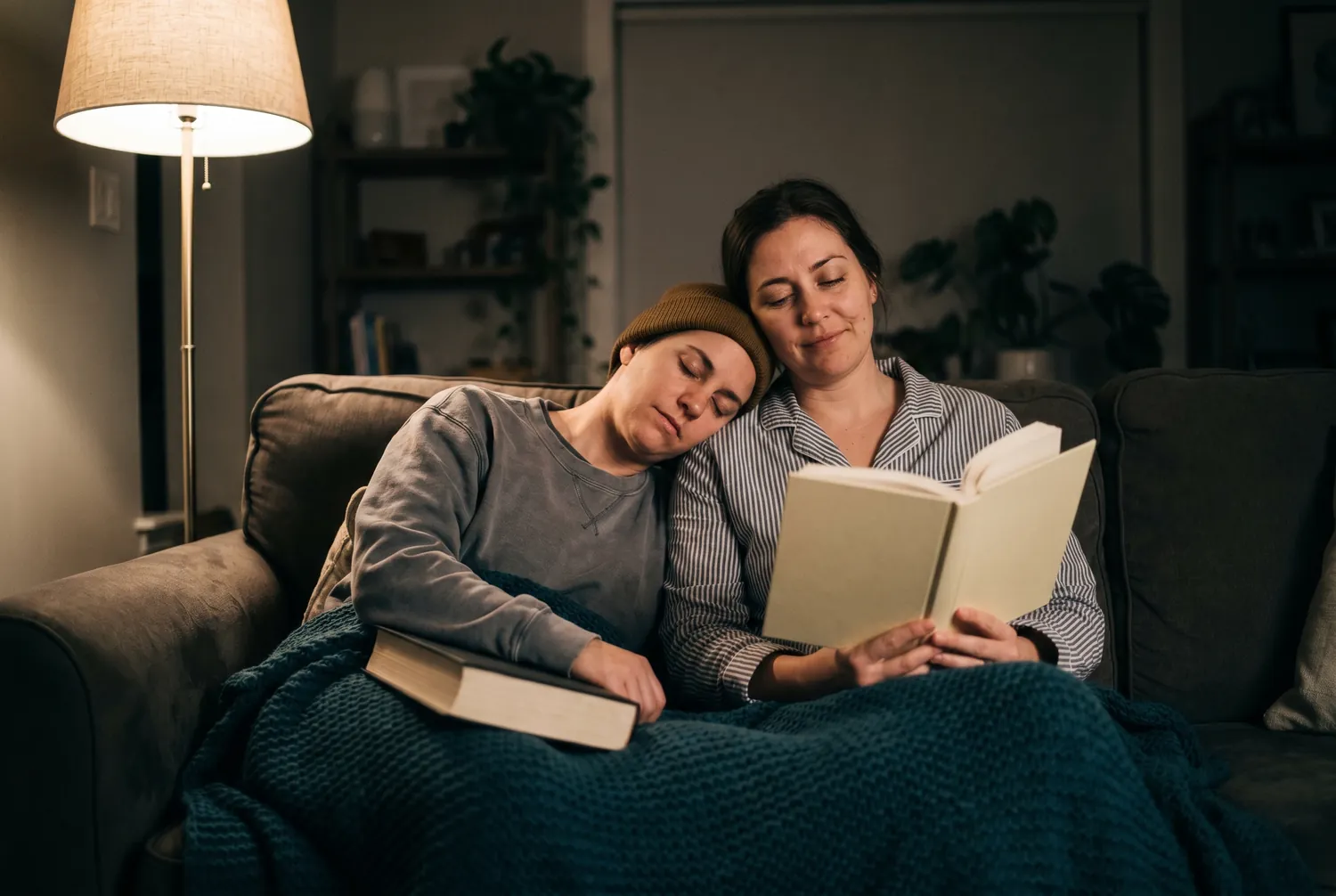 A couple winding down for the night reading under a blanket A couple winding down for the night reading under a blanket