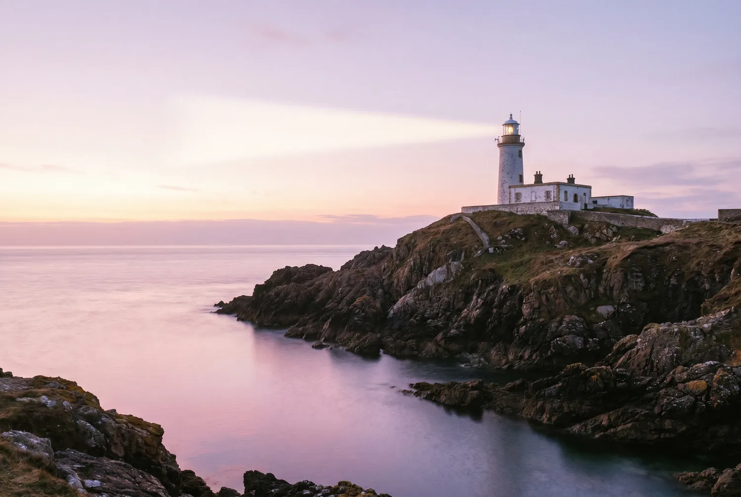 A white lighthouse on a headland at first light